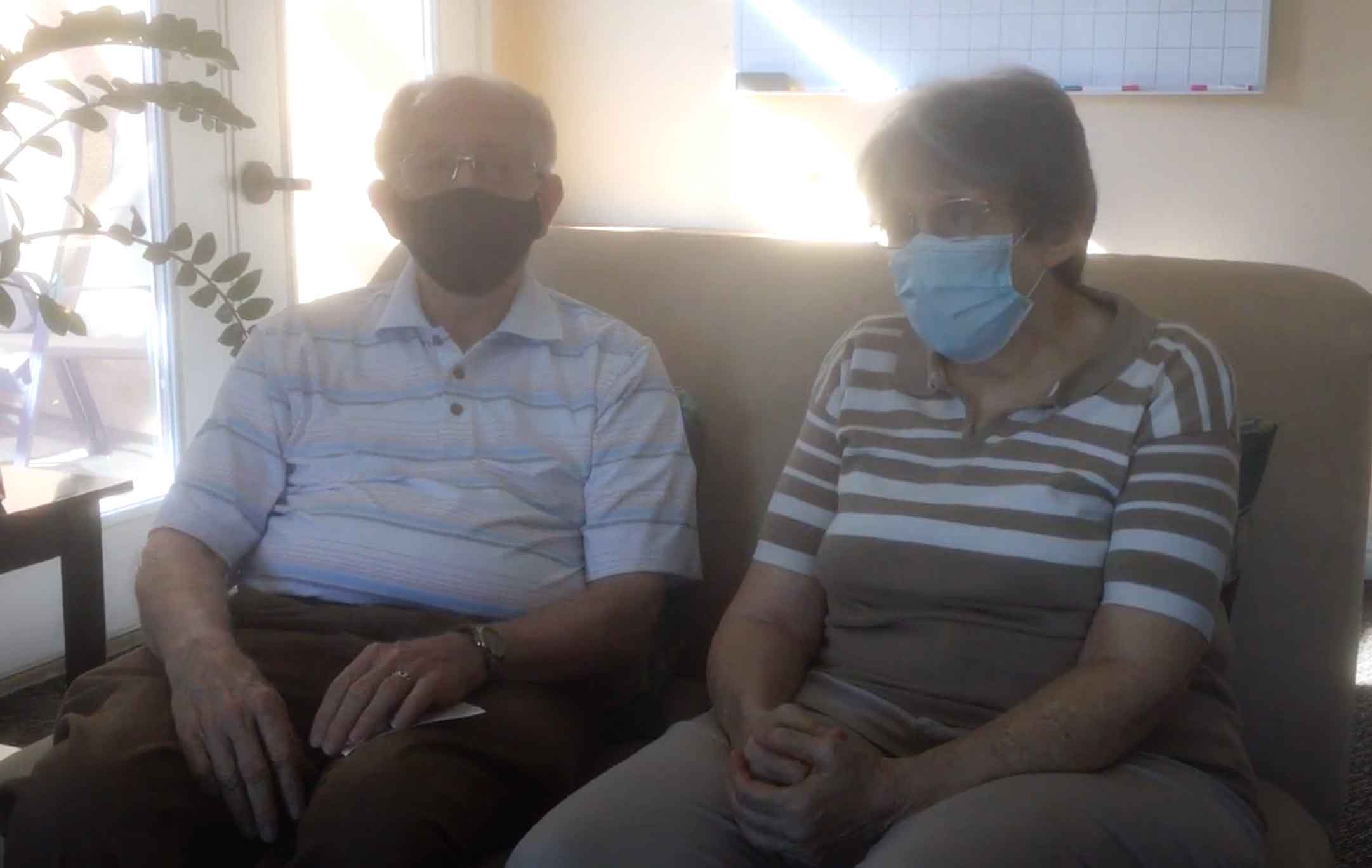 two heritage pointe residents sitting on couch with masks on female wearing brown and white striped shirt male wearing blue pink white striped shirt