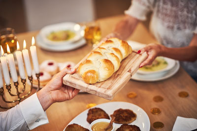 jewish holiday with jewish inspired meals with two older women passing bread to each other with hanukkah candles lit
