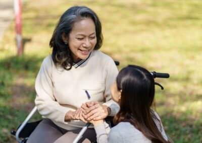 Senior woman in wheelchair holding hands with adult daughter