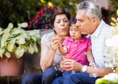 Grandparents sitting with their grandchild, blowing bubbles together outdoors